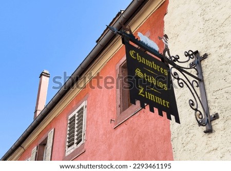 A rustic French auberge hotel with clear signage and room availability, seen in a low-angle view of its exterior architecture three languages same text, French, German, and English