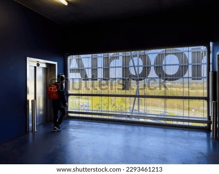 A silhouetted man stands alone in a empty airport parking transportation building, looking at the view while waiting for an elevator. Adventure awaits with his backpack in tow