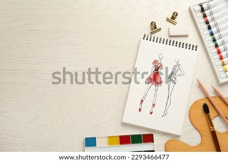 Sketches of different clothes in pad on white wooden table, space for text. Fashion designer's desk with stationery, flat lay