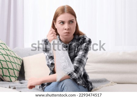 Angry woman popping bubble wrap on sofa at home. Stress relief