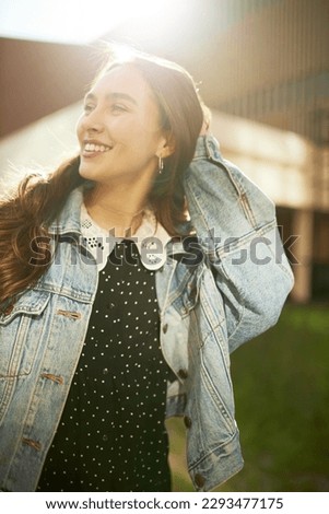 Vertical picture of gorgeous youthful elegant romantic-looking girl in trendy clothes posing in sun light touching her hair gently, smiling, enjoying warm weather and walk down city streets