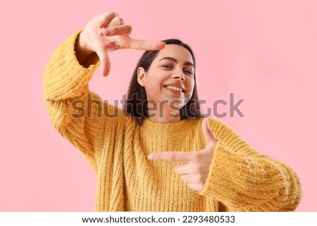 Beautiful young woman making frame with her fingers on pink background