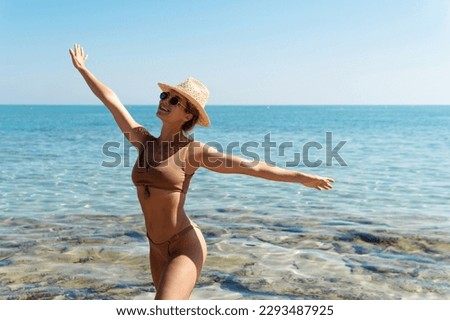 Carefree beautiful woman wearing brown bikini and straw hat during her beach vacation near blue sea.