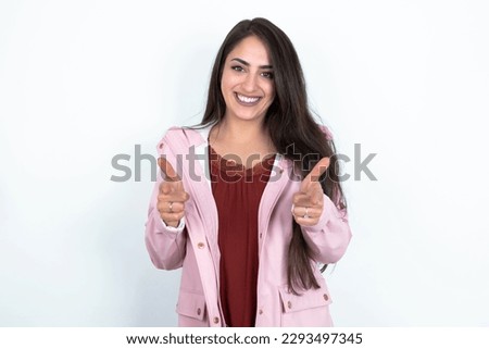 young brunette woman wearing pink raincoat over white studio background directs fingers at camera selects someone. I recommend you. Best choice