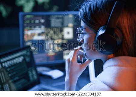 Focused on work. Young professional female hacker is indoors by computer with lot of information on displays.