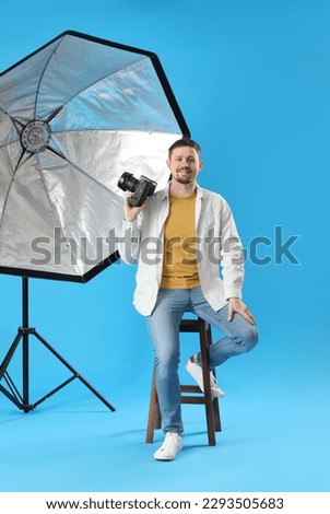 Male photographer with professional camera sitting on blue background