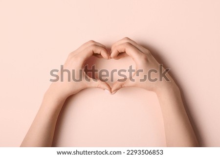 Woman making heart with her hands on beige background