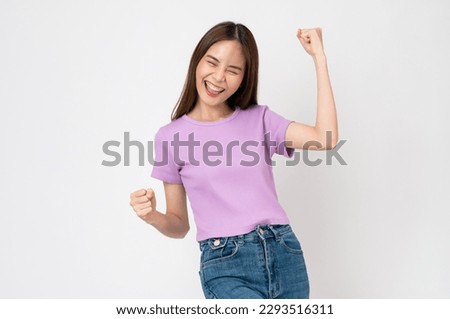 Beautiful Asian woman in a white t-shirt raises arms and fists clenched with shows strong powerful, celebrating victory expressing success. Royalty-Free Stock Photo #2293516311