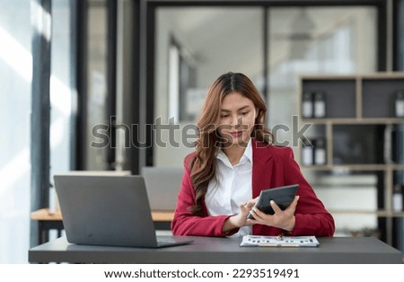 Beautiful asian businesswoman working on laptop and calculating with financial calculator from statistics data graphs, charts. Successful business results in modern office with joy.