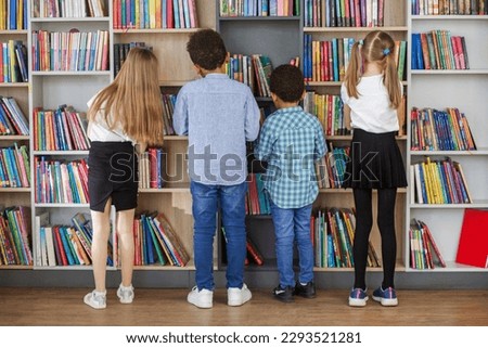 Four multietnic children look for books near bookshelves and read together in school library. Benefits of everyday reading.