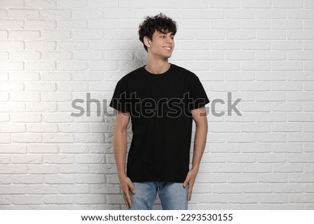 Man wearing black t-shirt near white brick wall. Mockup for design Royalty-Free Stock Photo #2293530155