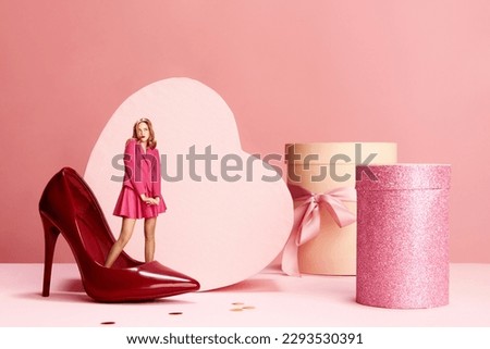 Beautiful, lovely young girl in cute dress and flirty look, standing in heeled shoes over pink background with present boxes. Concept of holidays, celebration, presents, sales. Copy space for ad