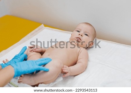 A pediatrician in gloves is examining a newborn baby on the couch. The doctor is checking the child for dysplasia. Royalty-Free Stock Photo #2293543113