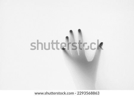 Defocused hand silhouette behind frosted glass in black and white mode, halloween concept
