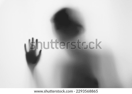 Defocused hand silhouette behind frosted glass in black and white mode, halloween concept

