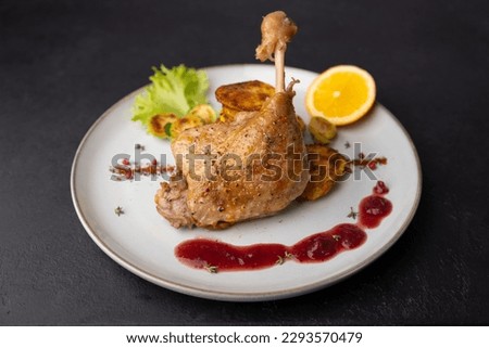 Duck leg confit with Brussels sprouts, baked potatoes, thyme, orange and lingonberry sauce. Traditional French cuisine. Selective focus, close-up, black background.