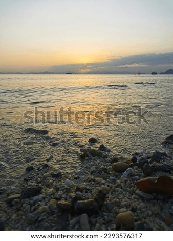Peaceful sunset above calm sea with part of the beach with rough sand and little rocks and shells in the bottom of the picture. Sunset vibes on tropical paradise island in Thailand.