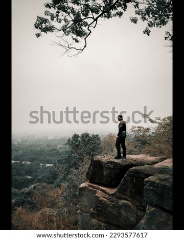 A man stands on a cliff and looks into the distance, a depressing environment in nature, a dried trees, bare stones burned by the sun, smoke