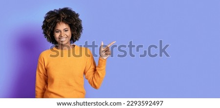 Cheerful attractive young african american woman with bushy hair and teeth braces pointing aside and smiling at camera, showing empty space over purple studio background, web-banner