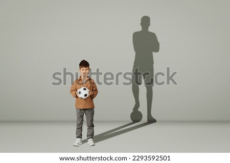 Positive caucasian 6 years old little child in casual with soccer ball and shadow of young soccer player isolated on gray background, studio, collage. Future with sports, kid dreams, lifestyle Royalty-Free Stock Photo #2293592501