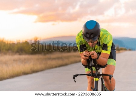  Close up photo of triathlete riding his bicycle during sunset, preparing for a marathon. The warm colors of the sky provide a beautiful backdrop for his determined and focused effort.
