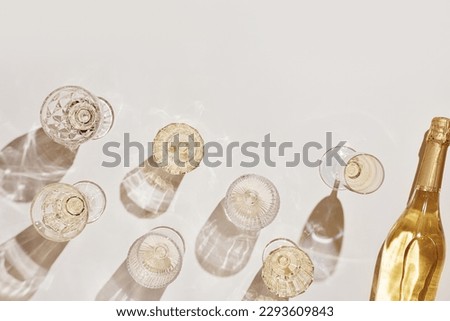 Summer party drinks flat lay, wine glasses with white sparkling wine and sunshine shadow on light table. Minimal pattern with beautiful wine glasses, above view still life, beige golden neutral color Royalty-Free Stock Photo #2293609843