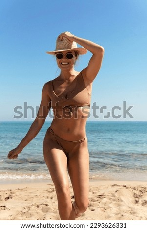 Carefree beautiful woman wearing brown bikini and straw hat during her beach vacation near blue sea.