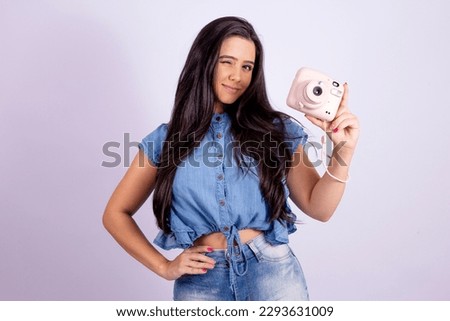 attractive girl holding a polaroid camera smiling at the viewer