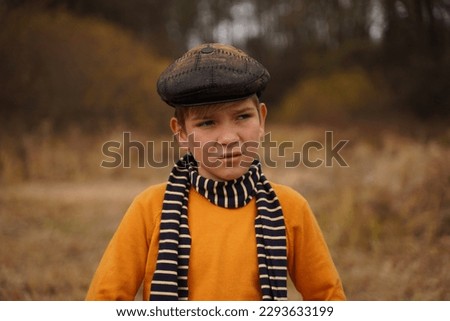 Portrait of a cute teenager in a retro cap and a striped scarf against the backdrop of an autumn forest