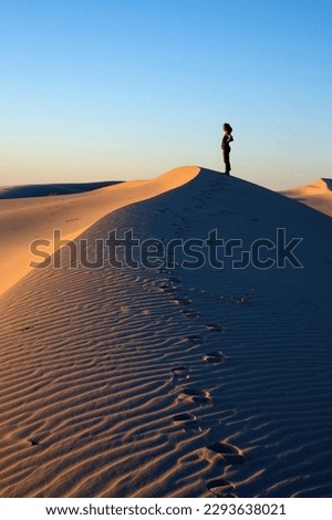 A woman walking on a desert dunes with a sunset light