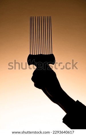 dark silhouette of male hand gently holding barber metal hair styling pik afro pick hair comb
