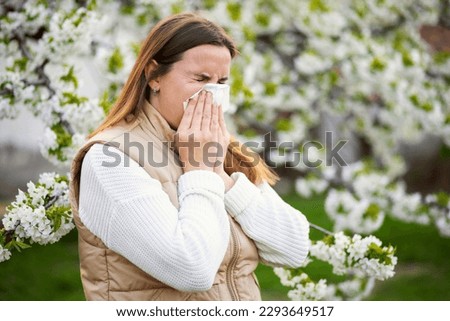 Sneezing woman with a nose wiper among the flowering trees in the park Royalty-Free Stock Photo #2293649517
