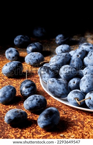 Fresh black plums on a white plate against dark orange background. Low key food still life photography