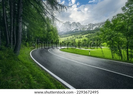 Road in green forest in rainy summer day. Dolomites, Italy. Beautiful mountain roadway, tress, grass, high rocks, blue sky with clouds. Landscape with empty highway through the wood in spring. Travel	 Royalty-Free Stock Photo #2293672495