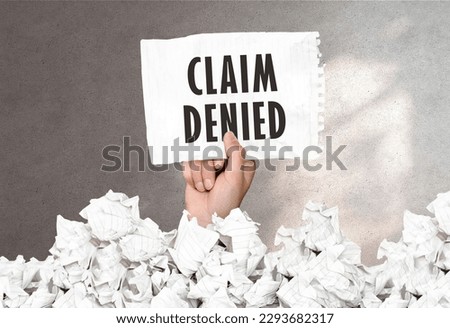 Hand holds a piece of paper with text CLAIM DENIED on a gray wall background