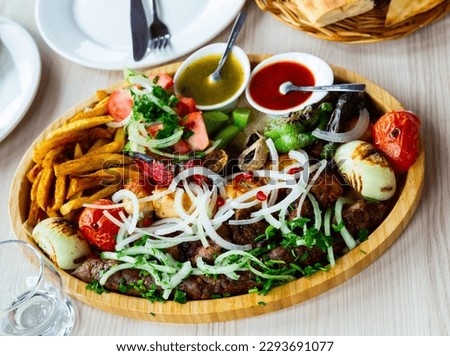 Dish with a appetizing assorty of Georgian cuisine of delicious shish kebab, french fries, baked vegetables, mushrooms,..peppers, fresh tomatoes, tkemali sauce, pita bread and sprinkled with chopped Royalty-Free Stock Photo #2293691077