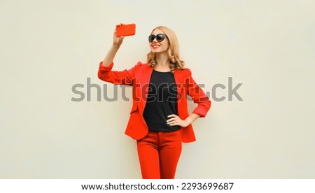 Portrait of beautiful smiling elegant lady woman taking selfie with smartphone wearing red business blazer on white background