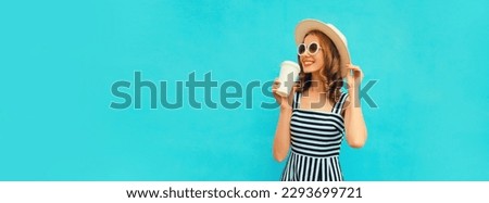 Portrait of happy smiling young woman drinking fresh juice or coffee wearing summer straw hat, dress on blue background