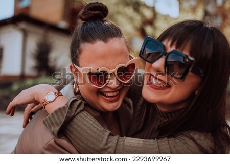 Two young women embrace each other emotionally outside on a sunny day while wearing sunglasses Royalty-Free Stock Photo #2293699967