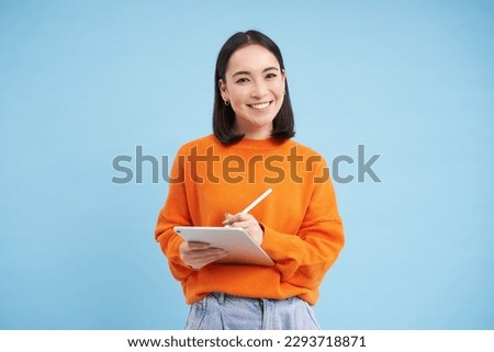 Portrait of young Chinese woman, teacher or student with digital tablet and pencil, writing, taking notes, doing her homework, standing over blue background.