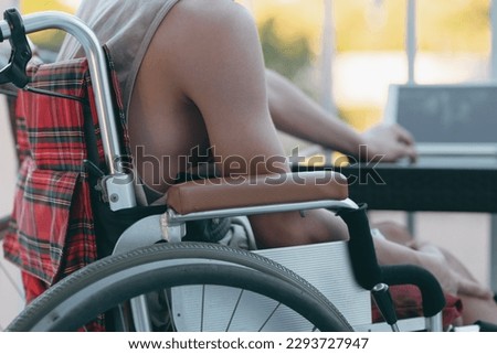 Young man with disability wear a tank top to cool off in the summer. Sit on wheelchair using laptop with a fan in the house,hospital,school,nursery, Taking care of health to suit the heat air.