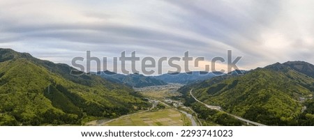 Panoramic aerial view of dramatic clouds over rural village in valley at sunset