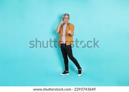 The attractive senior Asian man with yellow shirt standing on the green background.