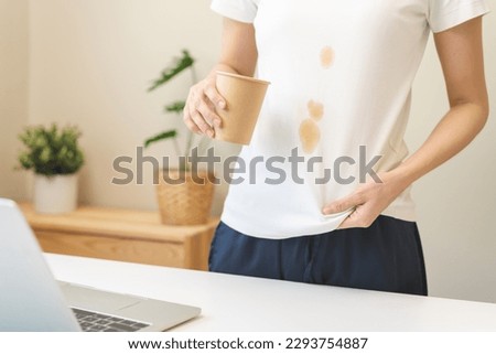 Cloth stain, disappointment asian young woman clumsy with hot coffee, tea stains on shirt, hand show making spill drop on white t-shirt, spot dirty or smudge on clothes at home, isolated on background Royalty-Free Stock Photo #2293754887
