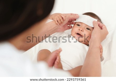 mother putting cool fever jel pad on forehead of happy sick baby  Royalty-Free Stock Photo #2293759361