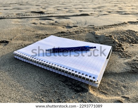 A coiled scribbler notebook with a pen on it on a beach as a concept image for relaxation and journaling Royalty-Free Stock Photo #2293771089