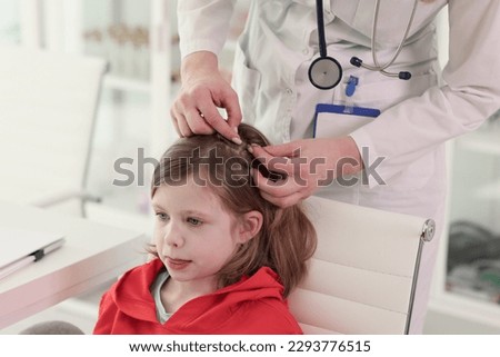 Therapist looks for insects in hair of little patient. Specialist in uniform does regular checkup of health and body of schoolgirl in clinic