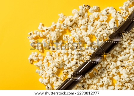 Scattered delicious popcorn and film stock on yellow background.