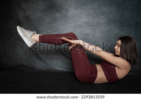Caucasian slim girl in red sportswear make morning stretching exercises at blackstudio background. Fitness as active lifestyle