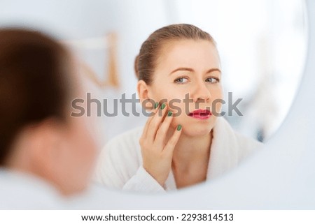 Unhappy young woman looking in the mirror and touching wrinkles on her face. Royalty-Free Stock Photo #2293814513